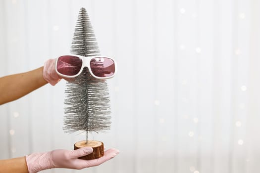 Woman's hands in gloves hold a decorative Christmas tree with protective glasses for laser hair removal. Concept of beauty, hair removal, depilation, epilation, smooth skin without hair, health.