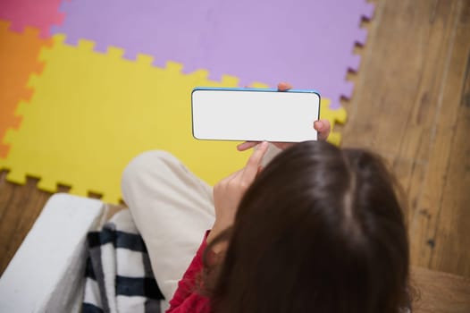 View from above of little kid's hands holding smart mobile phone with blank white empty digital touch screen. Mockup. Copy space for mobile application or advertising text. People. Wireless technology