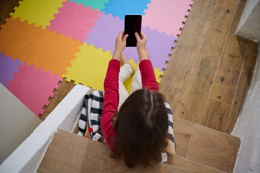 View from above of little kid's hands holding smart mobile phone with blank black empty digital touch screen. Mockup. Copy space for mobile application or advertising text. People. Wireless technology