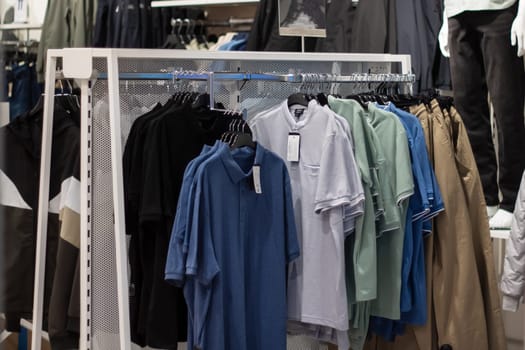 A row of Fashion design shirts, including Denim and Sportswear in Electric blue, are hanging on Clothes hangers in a Retail store