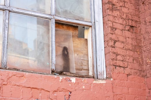 A broken window with brown wood fixture adds character to the brick wall facade, highlighting the tints and shades of the building material