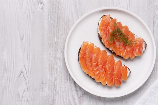 Rye sandwich with salmon and cream cheese on white wooden table, with copy space for text.