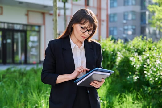 Portrait of business mature confident successful woman with digital tablet outdoor, educational office building background. Office employee school teacher insurance banking law firm real estate agent