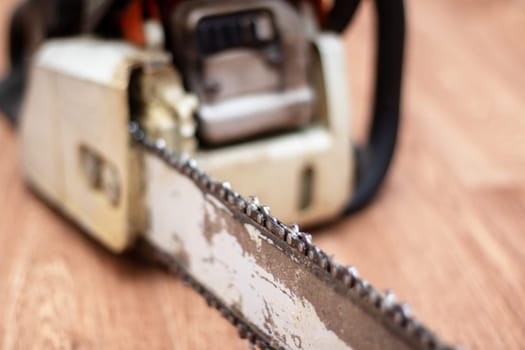 A chainsaw is resting on a hardwood flooring. The machine is powered by gas and is commonly used in automotive tire and wheel systems. It has metal parts