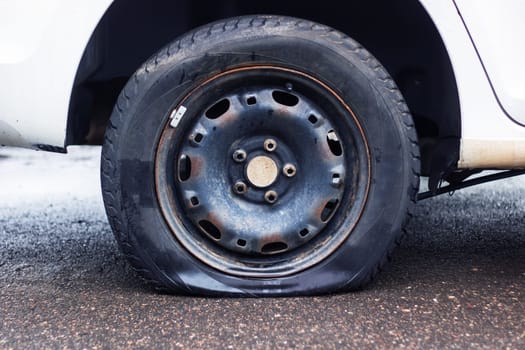 A car with a flat automotive tire on the side of the road, showing its alloy wheel and locking hubs. The tread made of synthetic rubber is visible, with the hubcap missing