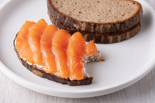 Rye sandwich with salmon and cream cheese on white wooden table.