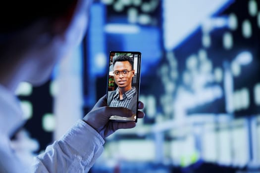 Close up of man in videocall with best friend while walking around city avenues at night, giving him work updates. Person uses laptop to show roommate dimly illuminated cityscape in blurry background