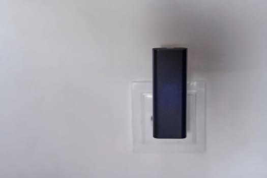 A black wi-fi router is plugged into a white electrical outlet on a grey wall in an art room, near a wooden door with a silver door handle