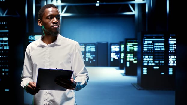 African american engineer in data center housing thousands of servers, storage devices and networking components providing vast amounts of computing resources. Expert doing hardware maintenance
