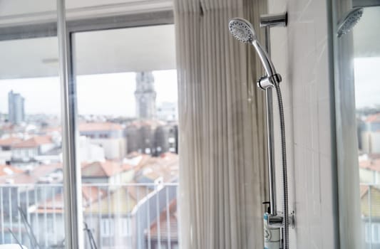 A shower stall with a glass shower door, metal handle, and composite material shower bar featuring a shower head and soap dispenser