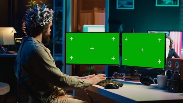 Computer engineer using EEG headset, starting mind upload process using green screen PC. Man using neuroscientific device to transfer consciousness into cyberspace with mockup monitors, camera A