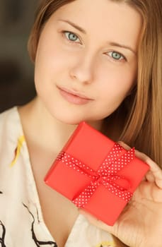 Happy smiling woman holding a red gift box, face portrait with natural make-up and holiday lifestyle at home concept