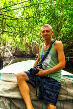 Young man male tourist with camera taking pictures on Boat safari trip through mangrove jungle forest in Bentota Ganga River Lake in Bentota Beach Sri Lanka.