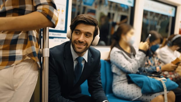 Smiling handsome male investor listening relaxing music while sitting on train. Professional business man enjoy listening music while using public transport to workplace. Blurred background. Exultant.