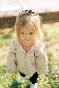 Little girl with a toy spider on her head stands on a green flowerbed. High quality photo