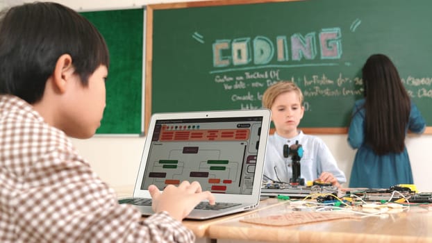 Asian boy coding program while caucasian friend fixing electric board at STEM class. Energetic student standing blackboard while writing coding engineering prompt and programing AI software. Pedagogy.