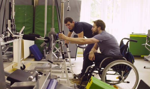 Young disabled man in wheelchair doing strength exercises for hands at the rehabilitation clinic