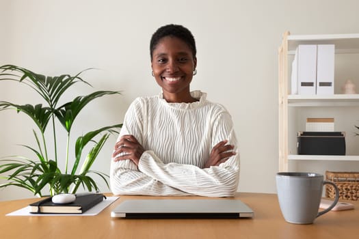 Happy young Black female entrepreneur at home office. African American woman looking at camera sitting at desk. Working at home concept.