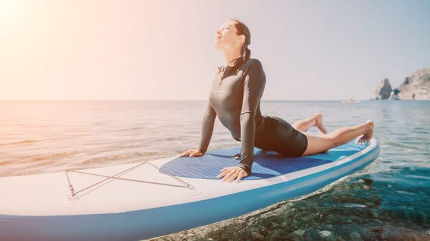 Woman sup yoga. Middle age sporty woman practising yoga pilates on paddle sup surfboard. Female stretching doing workout on sea water. Modern individual hipster outdoor summer sport activity