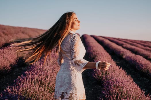 Close up portrait of young beautiful woman in a white dress and a hat is walking in the lavender field and smelling lavender bouquet.