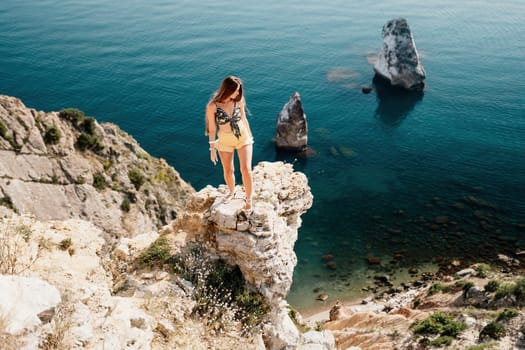 Woman travel sea. Happy tourist taking picture outdoors for memories. Woman traveler looks at the edge of the cliff on the sea bay of mountains, sharing travel adventure journey.