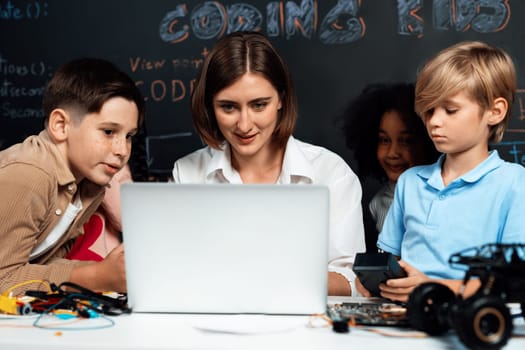 Teacher coding to demonstrate children how to code robots in the STEM class. Children fun to watch how teacher coding with confident only boy in blue shirt taking note with serious look. Erudition.