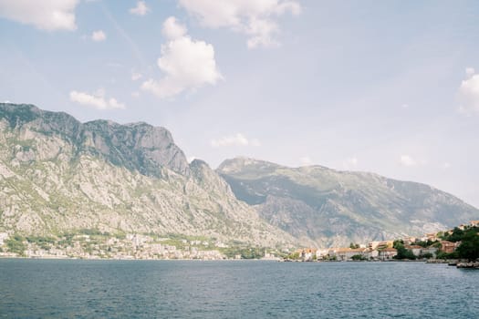 View from the sea to the coast of an ancient town with red roofs against the backdrop of a mountain range in a light haze. High quality photo