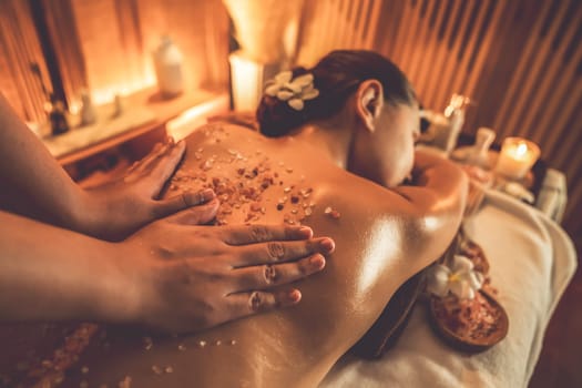 Woman customer having exfoliation treatment in luxury spa salon with warmth candle light ambient. Salt scrub beauty treatment in Health spa body scrub. Quiescent