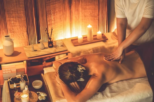 Caucasian woman customer enjoying relaxing anti-stress spa massage and pampering with beauty skin recreation leisure in warm candle lighting ambient salon spa at luxury resort or hotel. Quiescent