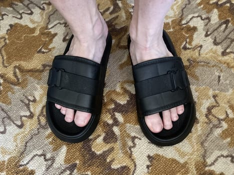 A man stands in black flip-flops on the the carpet