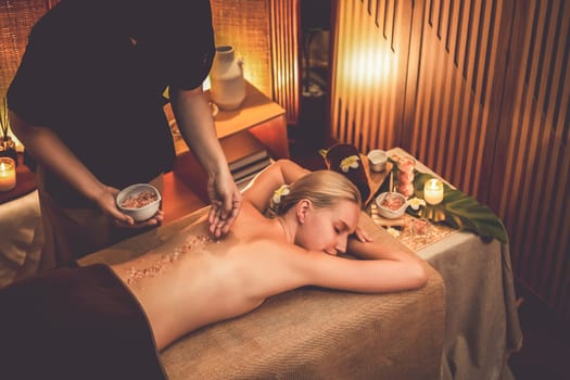 Woman customer having exfoliation treatment in luxury spa salon with warmth candle light ambient. Salt scrub beauty treatment in Health spa body scrub. Quiescent