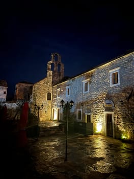 Courtyard of an old stone church with a bell tower at night in the illumination of lanterns. High quality photo