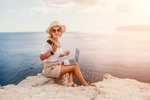 Digital nomad, Business woman working on laptop by the sea. Pretty lady typing on computer by the sea at sunset, makes a business transaction online from a distance. Freelance remote work on vacation