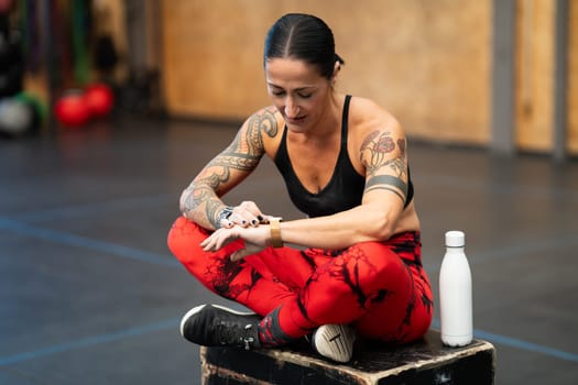 Female athlete sitting on a box using a smart watch after training in a cross training center