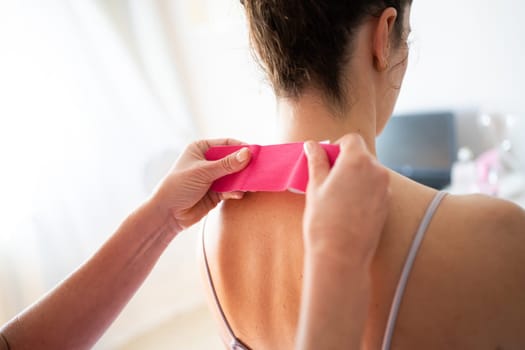 Back view of crop anonymous female receiving osteopathic and therapeutic treatment with kinesiology tape at back of neck while in modern clinic