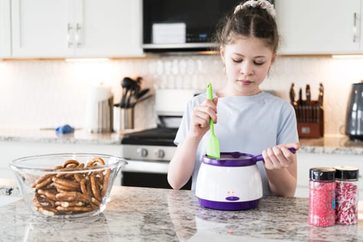 With focused attention, this budding culinary artist dips pretzels into a pot of melted chocolate, creating sweet delights in the warmth of a well-lit home kitchen.