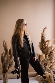 A crazy woman photographer, a blonde with a camera, happy and smiling in the production studio. Wearing a black clothes on a brown background