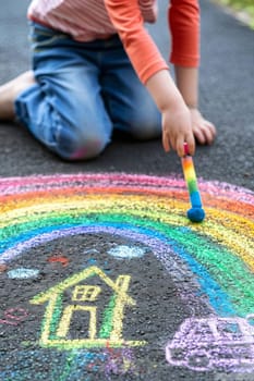 The child draws a house and a rainbow on the asphalt with chalk. Generative AI,