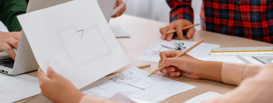 Skilled architect drafts blueprint on paper while male engineer works on laptop in architectural office. Professional engineer and architect collaborate on architectural project. Closeup. Delineation.