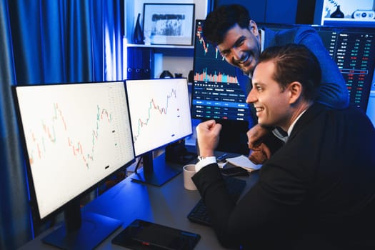 Cheerful two stock exchange traders raising fist up for digital currency achievement focusing on dynamic data background. Successful investors earning high profit analyzed by market graph. Sellable.