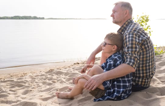 Father's day concept. Father and son sit together on the river bank and look into the distance