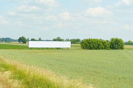 A sizable billboard positioned amidst a vast field of grass under the sky.