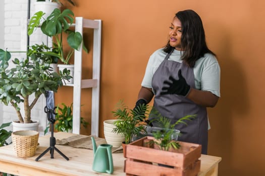 African american florist blogger filming tutorial video about transplanting plants in home garden. Make video vlog with mobile phone concept