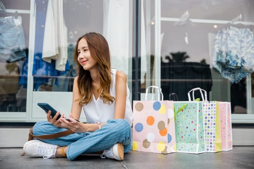 Efficient shopping in action ,young woman making purchases with her smartphone and credit card while sitting on the ground with shopping bags. E-commerce and convenience at its finest