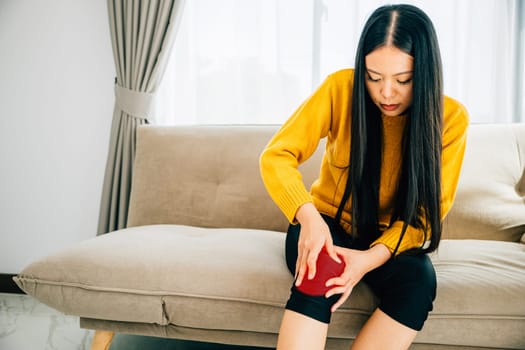 Close-up of a woman on sofa holding her painful knee indicating chronic tendon arthritis. Depicting Health Care and Medical Concept emphasizing tendon inflammation and pain.