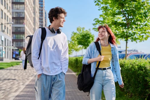 Talking walking friends, guy and girl, university college students walking together along street of modern city. Youth 19-20 years old, friendship, communication, urban lifestyle concept