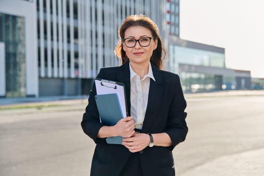 Outdoor portrait of middle aged business woman agent manager holding digital tablet clipboard, on street of modern city. Business marketing work financial services rental real estate sales insurance