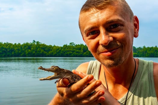 Man tourist with baby crocodile alligator in his hands at Bantota Ganga river in Bentota Beach Galle District Southern Province Sri Lanka.