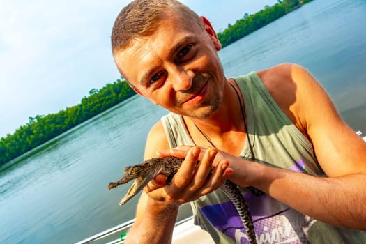 Man tourist with baby crocodile alligator in his hands at Bantota Ganga river in Bentota Beach Galle District Southern Province Sri Lanka.