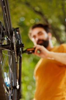 Image showing close-up view of bike rear derailleur and cogset being repaired and adjusted outside for leisure cycling. Detailed shot of young male cyclist checking tire as annual bike maintenance routine.
